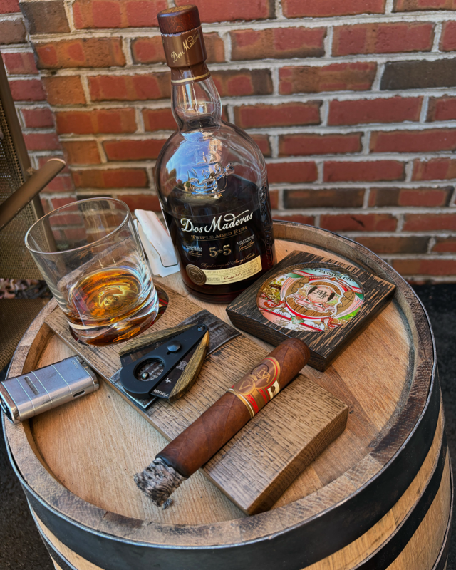 Rum, cigar, and handcrafted barrel-wood coasters resting on an authentic whiskey barrel top