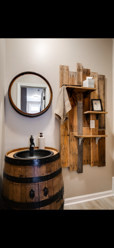 Barrel vanity sink with reclaimed wood shelving and barrel-hoop mirror in a finished bathroom